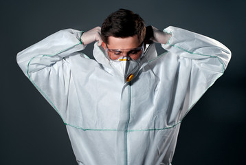 Male doctor or laboratory researcher is wearing a protective suit, a respirator and glasses are isolated on a dark gray background.