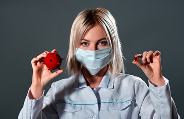A female doctor in a medical protective mask holds a 3D model of coronavirus infection in her hands...