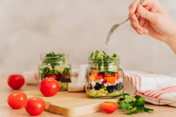 Healthy Homemade Jar Salad with cucumbers and tomatoes. Healthy food, Diet, Detox, Clean Eating or Vegetarian concept. the girl picks up a salad with a fork