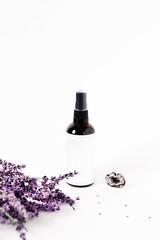 Glass spray bottle on white background surrounded by lavender bouquet and the crystal of quartz.