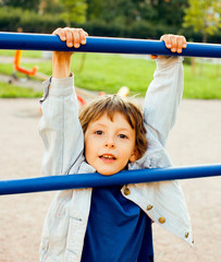 Fototapeta premium little cute real boy playing on playground, hanging on gymnastic ring cheerful