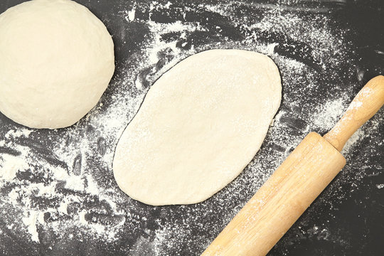 Dough and wood rolling pin on clean black background top view