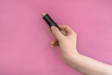 Highlighter for sculpting in a woman's hand on a pink background. Advertising.