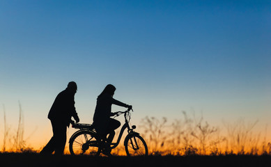 Fototapeta na wymiar Silhouette of a girl and man on the e-bike or electric bicycle on the sunset background. Country style, transportation in the village. Copy space.Travel, father and daughter.