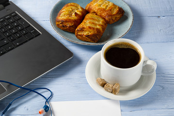 Laptop with cup of coffee and bakery on light blue old wooden table. Notebook with cup of fresh coffee in home office. Working from home concept