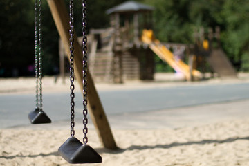 Two abandoned swings with an empty playground in the Background in the park during Lockdown because of corona pandemic
