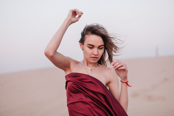 Fototapeta na wymiar portrait of a young slender girl in a red dress in the wind in the desert