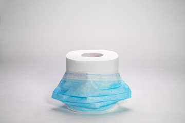 COVID-19. 2019 Novel Coronavirus (2019-nCoV) concept. A roll of toilet paper is standing on a white background in a blue protective medical mask