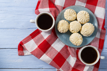Cup of americano coffee and homemade zephyr or marshmallow in a blue plate on light blue wooden background.