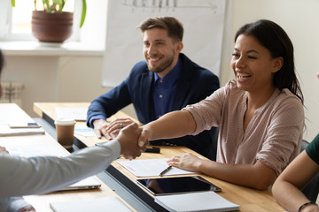 Happy laugh hr african american businesswoman shaking hand of applicant at interview. Diverse...