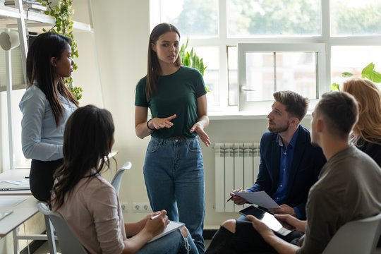 Serious female leader, mentor holding briefing for multiracial team interns in office, teaching students, plan to subordinates. Confident businesswoman at company meeting with diverse colleagues.