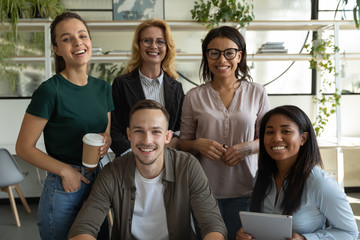 Portrait of happy smiling diverse mixed race employees team standing in office, holding cup of coffee and tablet, posing for company photo together, looking at camera.