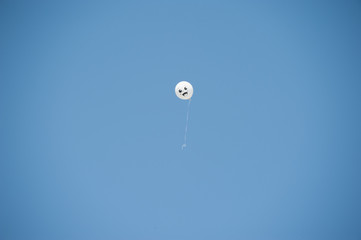 a lone flying white balloon with a painted smile