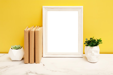Empty white frame mock-up with a home plants and books on the table on yellow background