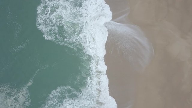 Flying over a sandy beach. Waves break on a sandy beach on the Atlantic coast, aerial View. Nazare, Portugal. (raw video).