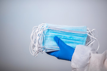 COVID-19. 2019 Novel Coronavirus (2019-nCoV) concept. A healthcare professional is holding a pack of sterile medical masks with disposable blue gloves. Protective antiplague suit.