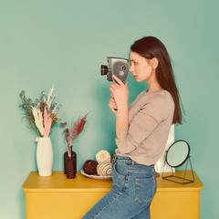 portrait of a girl in blue jeans with a retro camera th in hands on a turquoise background