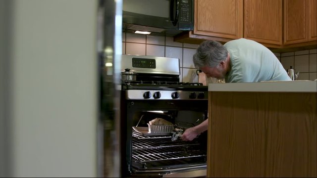 A mature man trying the popular pastime of bread making during stay at home social distancing mandates due of COVID19 smiles as he removes his first homemade loaf from the oven.