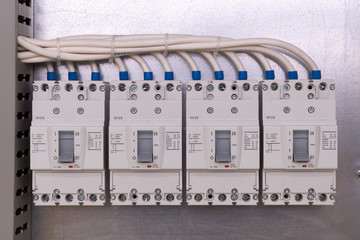 Four large power circuit breakers are mounted on a panel in a row in the electrical Cabinet. Cables are connected to the switches. The wires are carefully laid in a perforated cable channel.