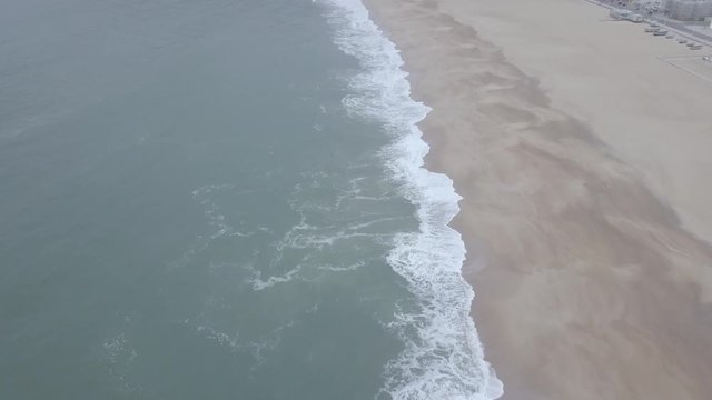 Flying over a sandy beach. Waves break on a sandy beach on the Atlantic coast, aerial View. Nazare, Portugal. (raw video).