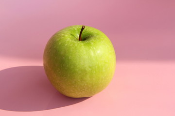 Green yellow apple on a pink background. Juicy ripe beautiful fruit.