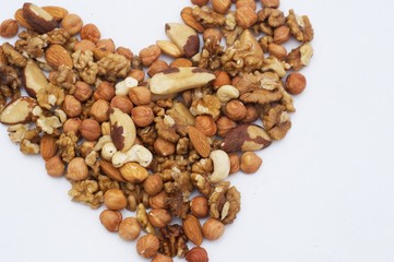 Different nuts in form of heart. Brazil nuts, walnuts and hazelnuts on white wooden background. Healthy food concept. Vegetarian food. Fresh food 