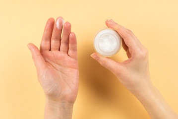 Hand cream and woman hands on a beige background.