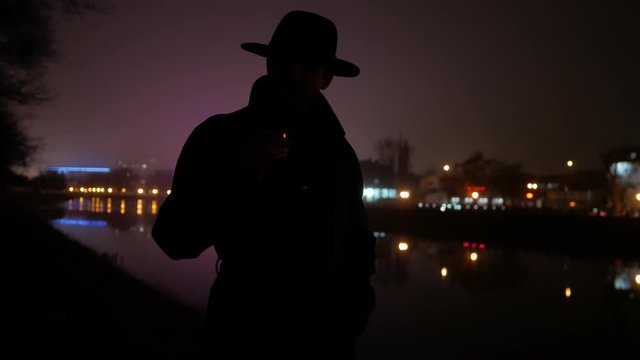 silhouette of a man with hat smoking cigarette in the city