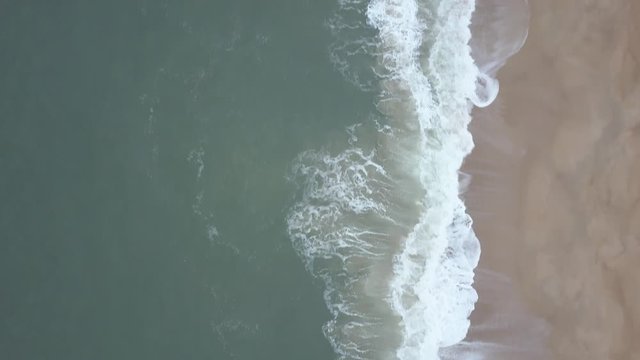 Flying over a sandy beach. Waves break on a sandy beach on the Atlantic coast, aerial View. Nazare, Portugal. (raw video).