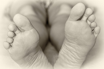 The girl is lying on a bed on a white sheet. Close-up foot shot. Rest after a hard day. Black and white photo, high key. Picture taken in Ukraine, Kiev region.