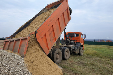 A dump truck unloads sand at a construction site. © Niko_Dali