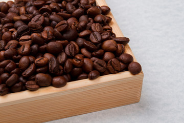 Close up heap of roasted coffee beans in a wooden form. Isolated on white.