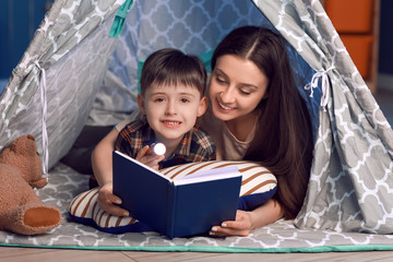 Woman and her little son reading book in play tent at night