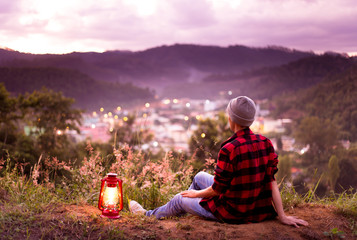 Fototapeta premium Person feeling free and enjoying life and watching the city lights with twilight sky. kerosene lamp on.