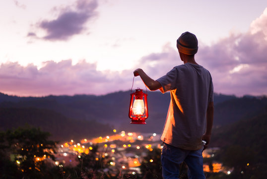 Young man feeling free with a kerosene lamp on, and watching the landscape with the twilight sky.