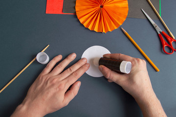 Paper Halloween Jack O'Lantern step-by-step instruction. Step 20: Person applies glue to a circle of white paper. DIY Halloween decoration theme. - obrazy, fototapety, plakaty