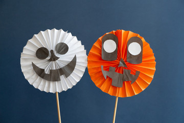 Obraz premium Two different folded paper decorations (smiling skull and Jack-o'-lantern) on the blue background. DIY Halloween decoration theme.