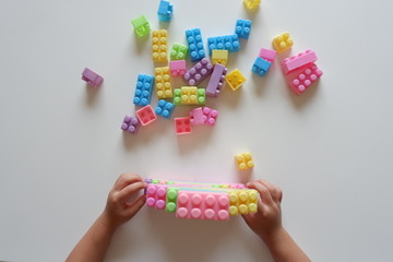 Close up of child's hands playing with colorful plastic bricks at the table. Toddler having fun and building out of bright constructor bricks. Early learning. stripe background. Developing toys