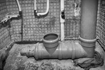 Toilet apartment in a multi-storey residential building in the city. Replacing an old iron sewer pipe with a new plastic one. Installation of the system. Black and white photography.