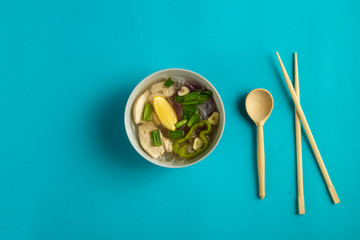 A light plate of Vietnamese Pho soup with chicken on a blue background.