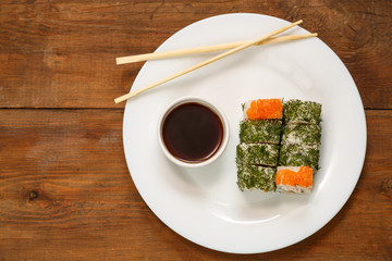 A set of rolls with dill and salmon on a plate with soy sauce and chopsticks.