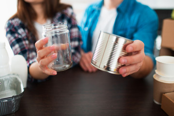 Close-up. Husband and wife are holding two tin cans in their hands. A young couple sorts trash in the kitchen. Young man and woman are sorting recyclables.
