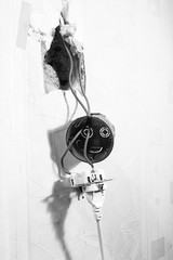 Repair of an electrical outlet in a city apartment. Visible insulated wires, disassembled power outlet. A hole has been made in the wall. Vertical frame. Black and white image.