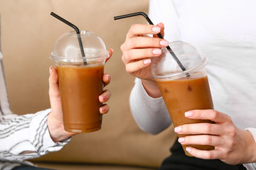 Women with cups of tasty iced coffee in cafe, closeup