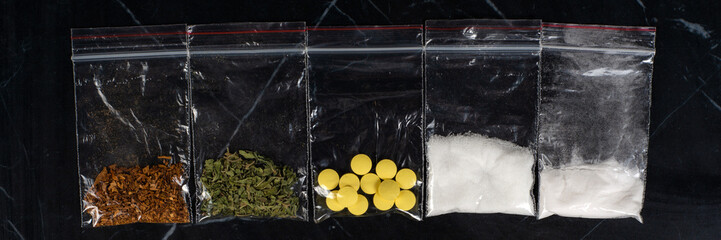 lethal concept: tobacco, weed, MDMA tablets, amphetamine crystals, heroin in plastic bags, on a dark background. Enhanced contrast, partial blur.
