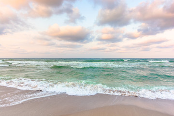 golden cloudy sunset above the green sea waters. waves crashing the sandy beach. clear horizon. changing windy weather