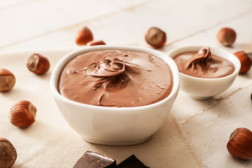 Bowl with tasty chocolate paste and hazelnuts on table