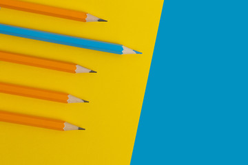 Blue pencil and orange pencils on a yellow paper background.