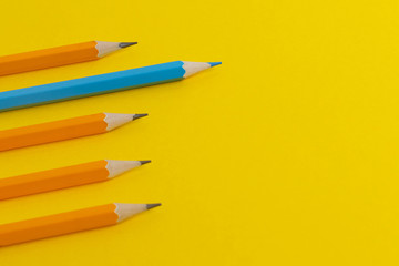 Blue pencil and orange pencils on a yellow paper background.
