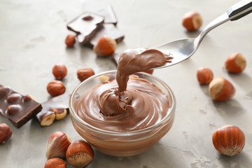 Bowl and spoon with tasty chocolate paste and hazelnuts on grunge background